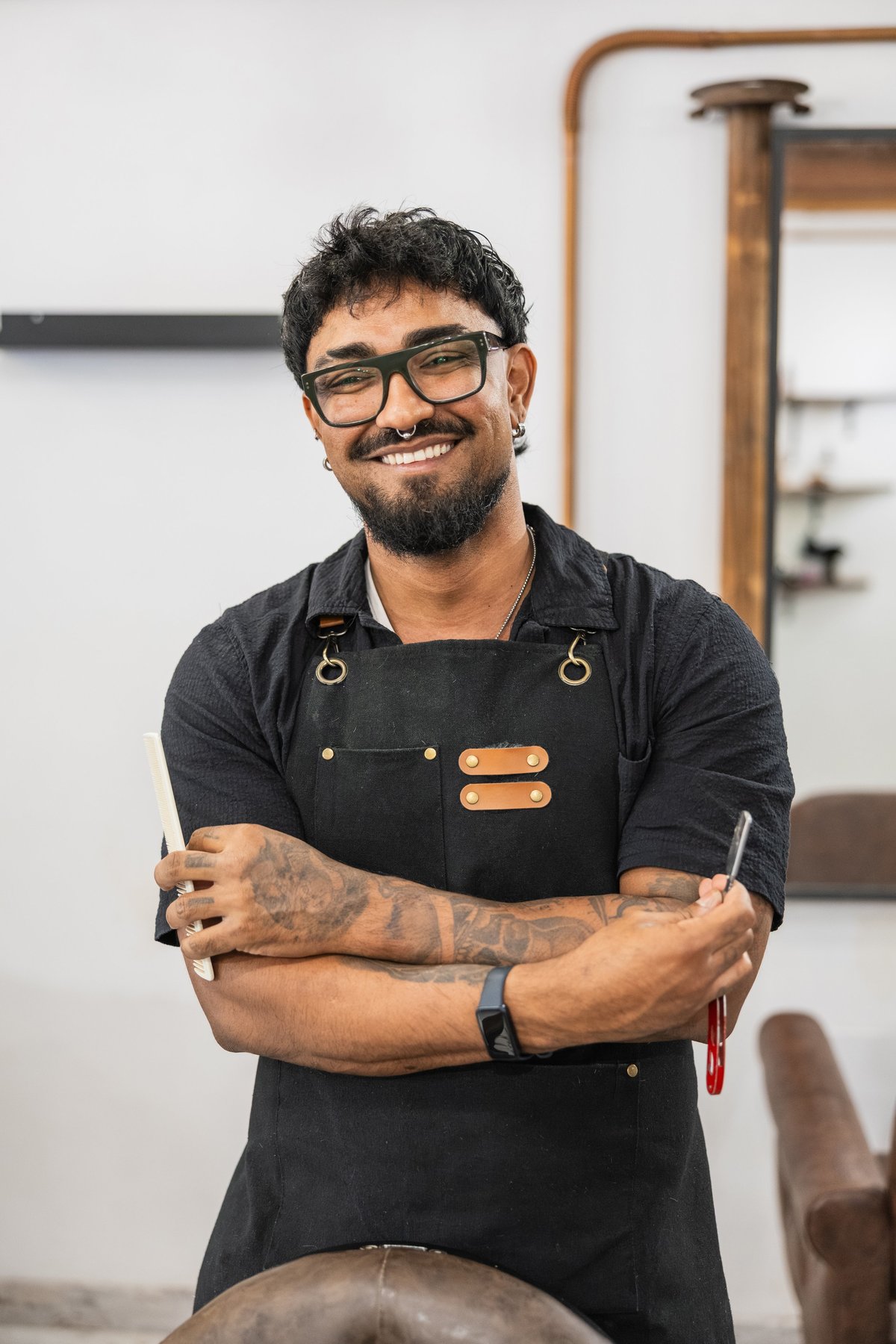 Happy barber wearing an apron and glasses, holding a razor and comb