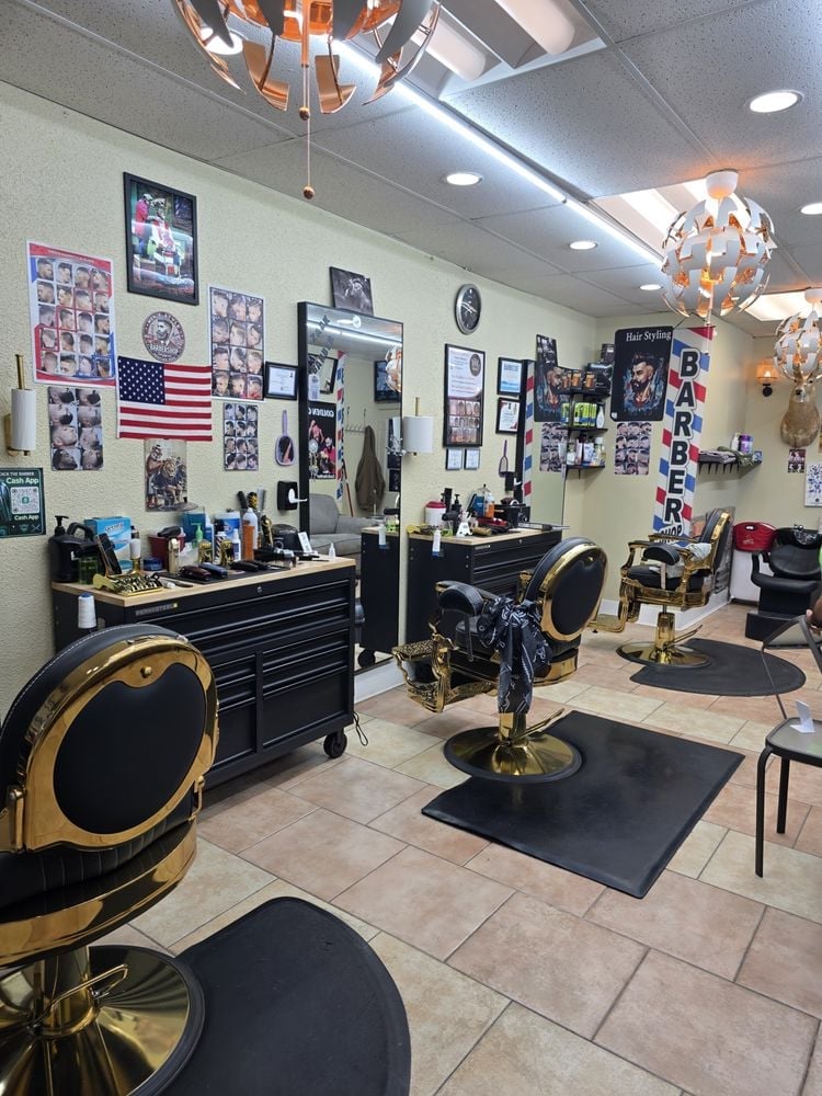 Modern barbershop interior with black and gold barber chairs, black tool cabinet, decorative mirrors, and sports photos on cream-colored walls