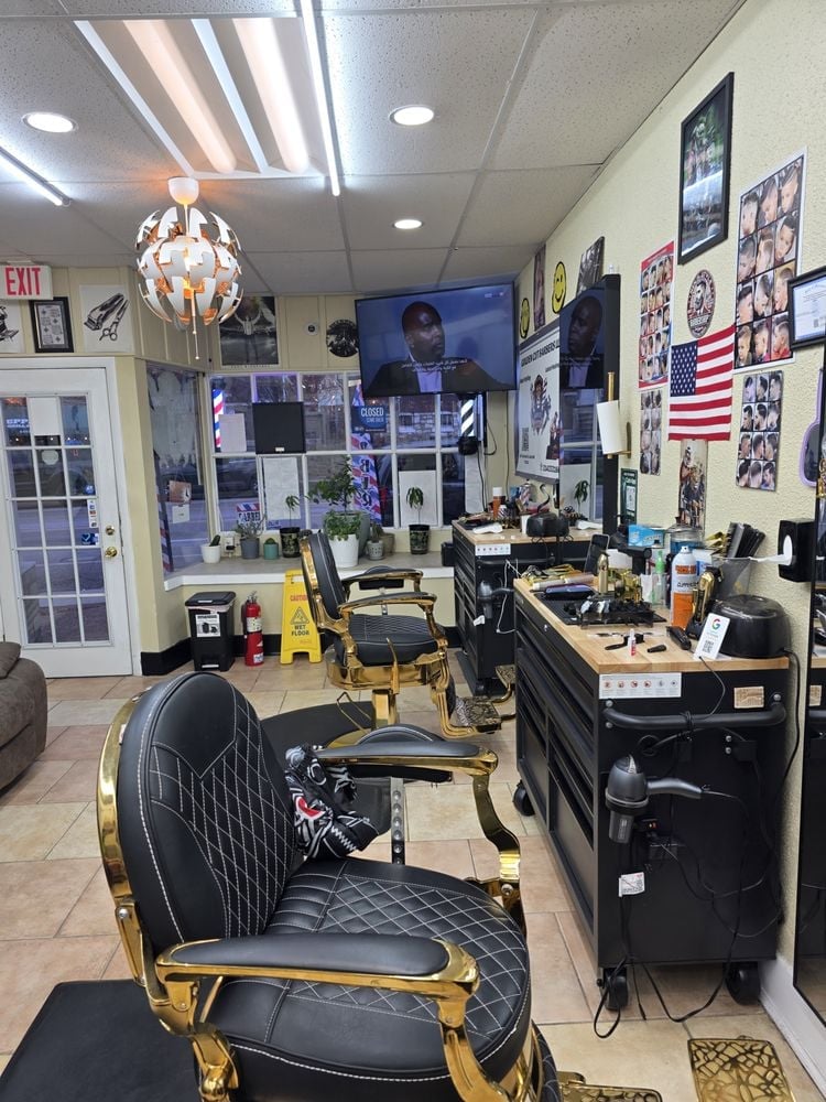 Interior of a barbershop with black and gold chairs, styling stations, and walls decorated with photos and an American flag